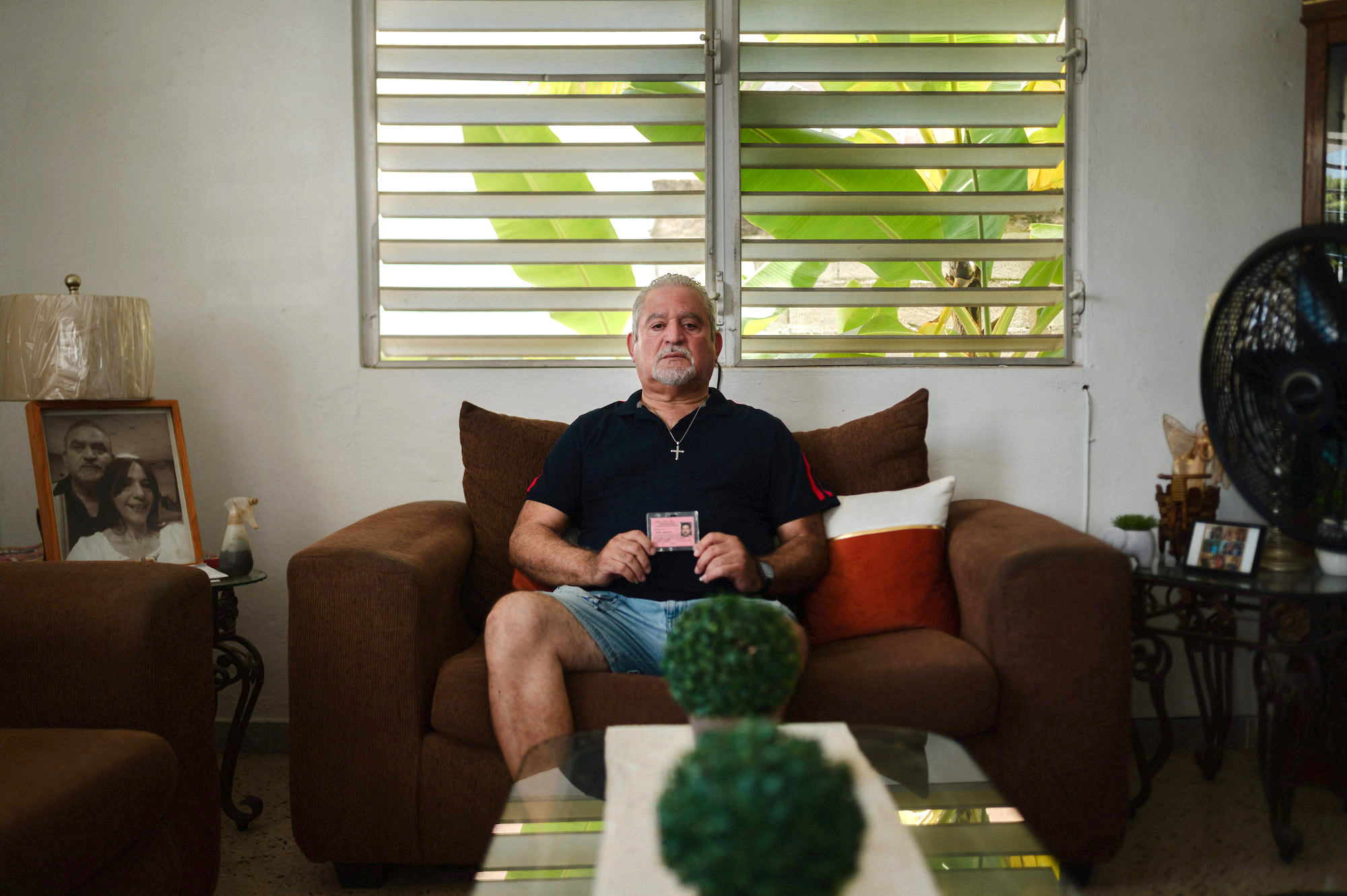 A man sits on a couch in his home holding a pink employee ID